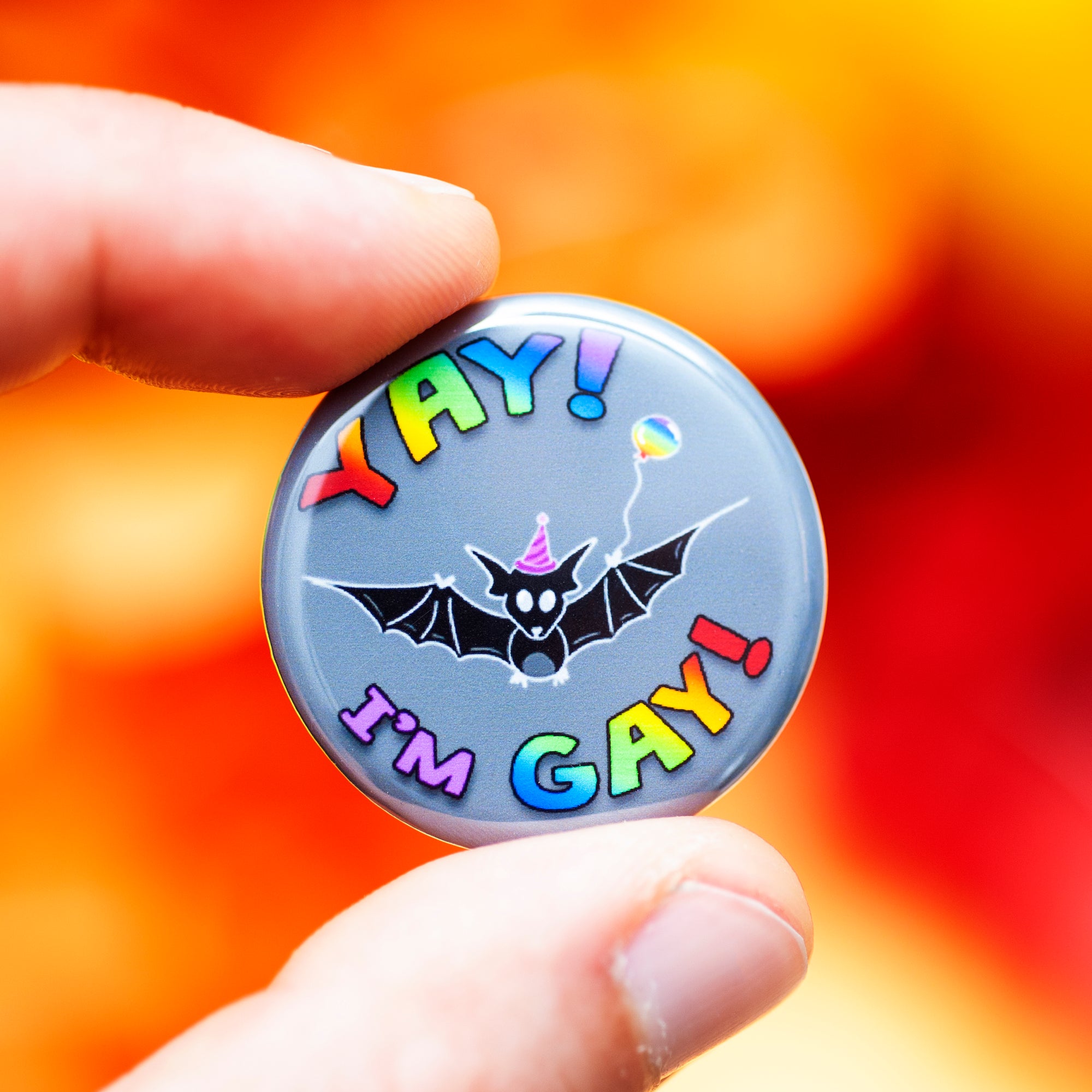 CQS "yay I'm gay" button held up against a red-orange background